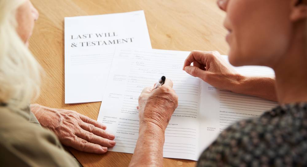 An elderly woman signs a Will with a younger woman present.