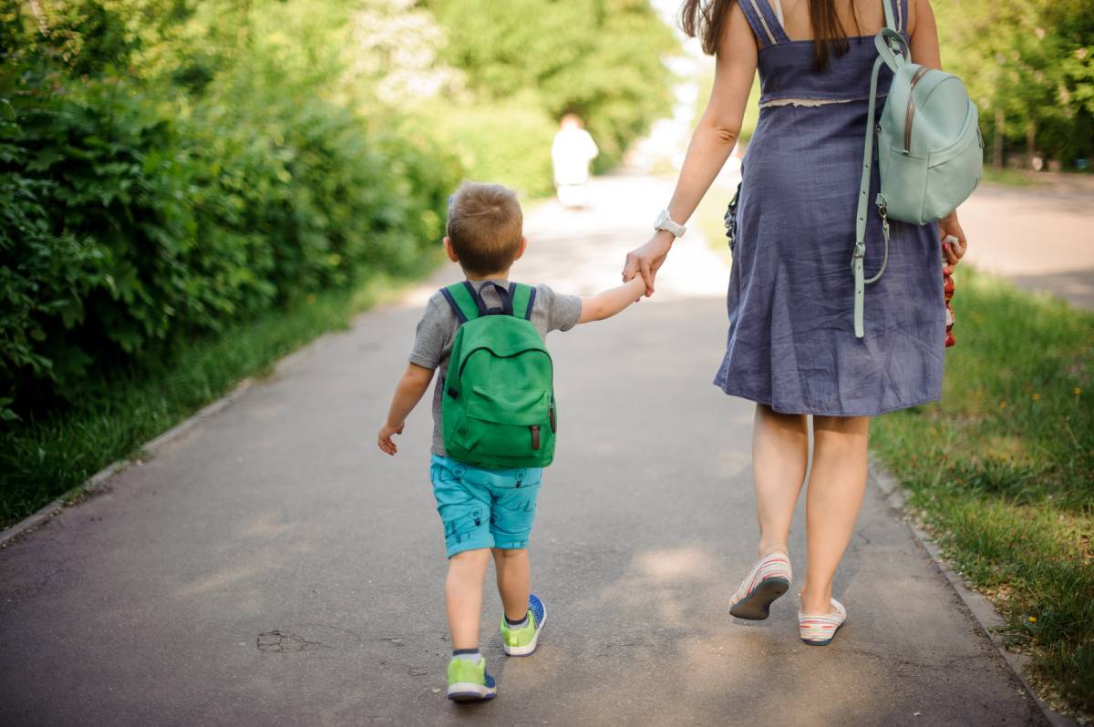 It's summer. A woman and a small child hold hands as they walk down a sidewalk.