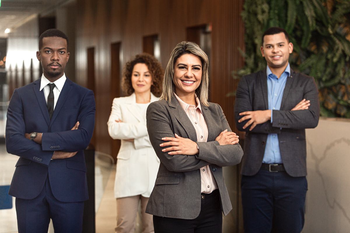 A group of lawyers stands in with their arms folded across their chests. One woman stands in the foreground with a bigger smile on her face than the others.