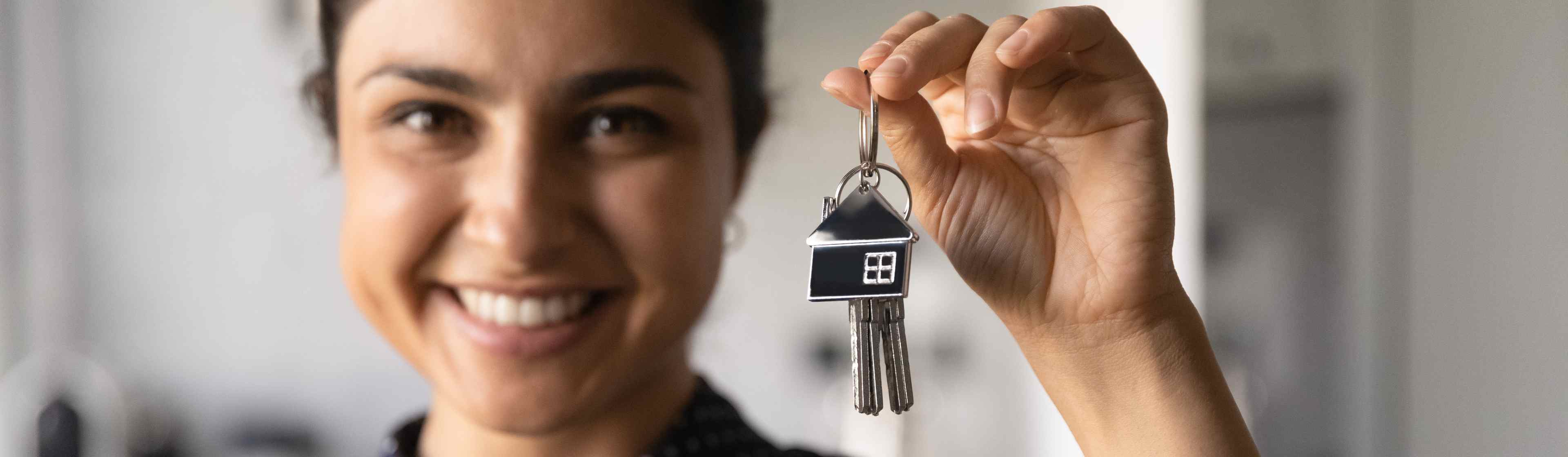 A female landlord smiles while holding up a set of keys with a keychain shaped like a house.