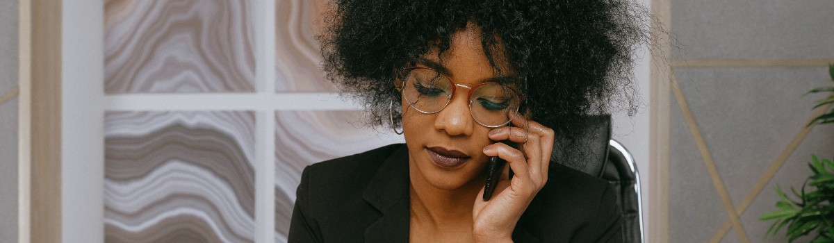 A woman wearing glasses is on the phone. Her expression is calm but focused. 