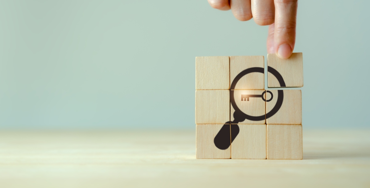 Someone places the last wooden block on a pile to complete a puzzle picture of a magnifying glass over a key.