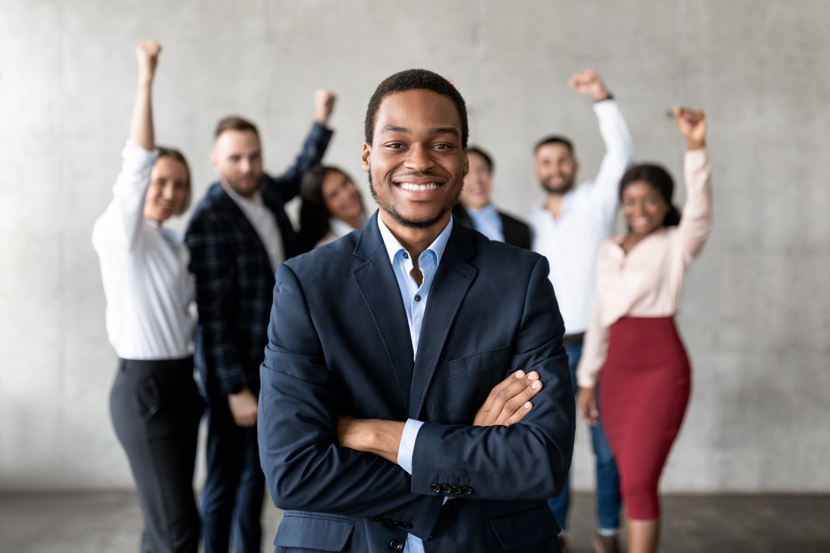 A young businessman stands in front of a business team who are cheering him on.