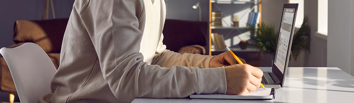 Person writing on a notepad while also working on their laptop.