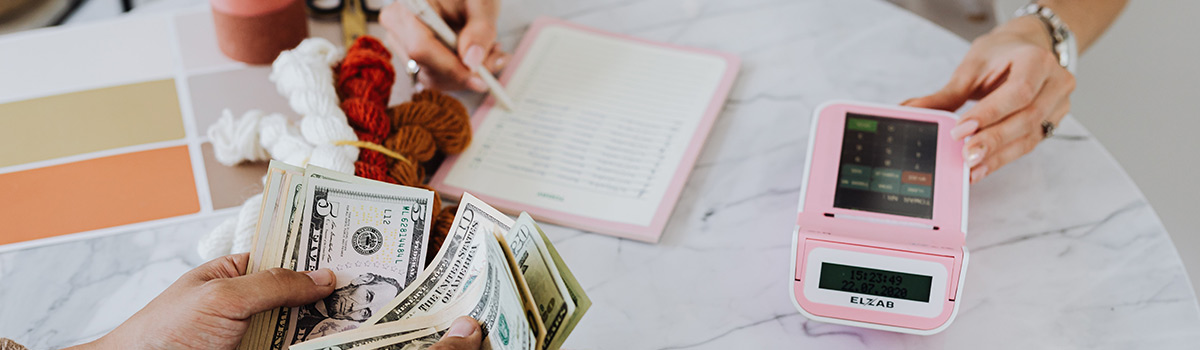 A person counting cash and a person checking sales on a point-of-sale system.