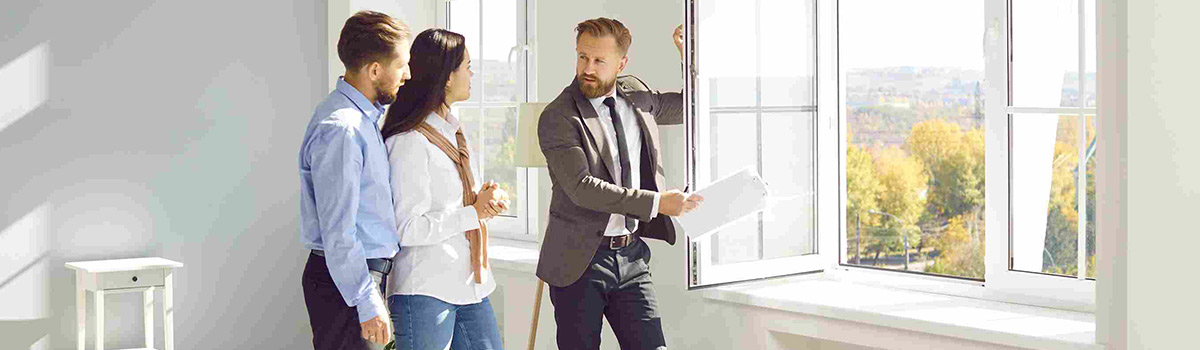 Man showing a couple a window inside the room of a home.