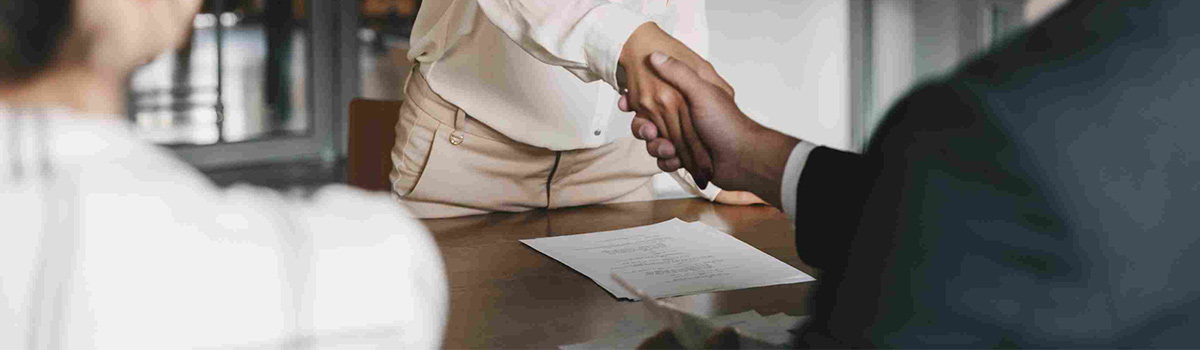 Two people shaking hands over a desk with papers on it.