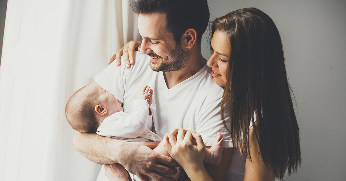 A young couple smiles as they cradle their newborn baby in their arms.