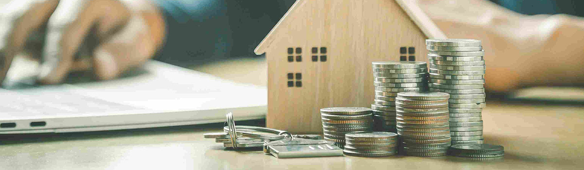 Miniature house next to stacks of coins and keys.